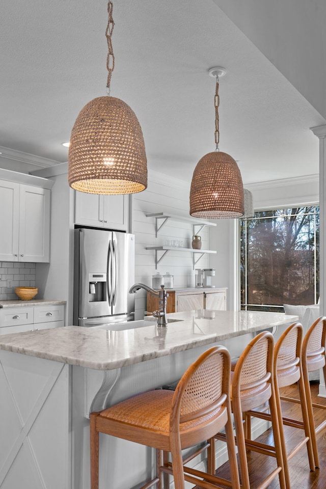 kitchen with stainless steel fridge with ice dispenser, pendant lighting, white cabinets, and tasteful backsplash