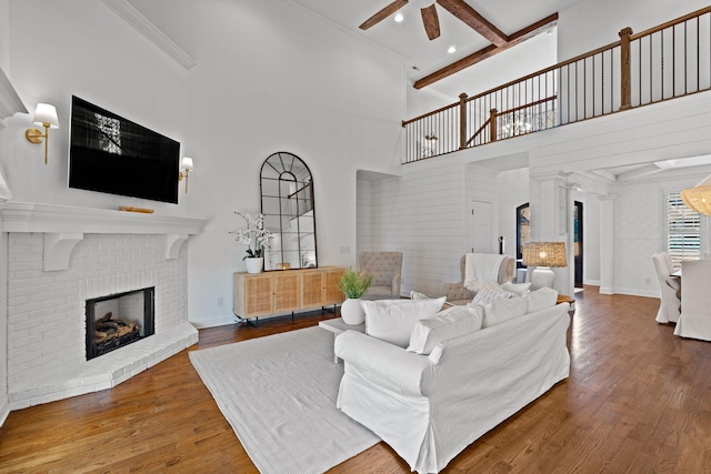 living room featuring a brick fireplace, ceiling fan, hardwood / wood-style floors, and beamed ceiling