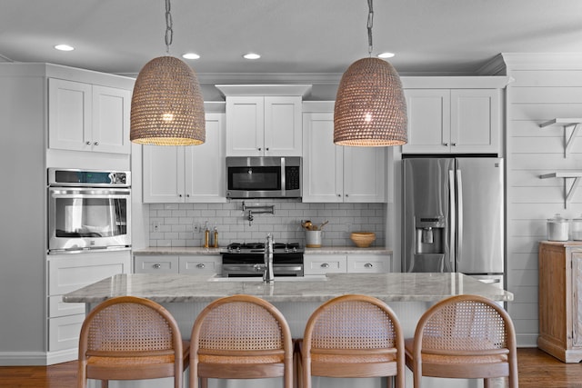 kitchen featuring hanging light fixtures, stainless steel appliances, white cabinetry, and light stone counters