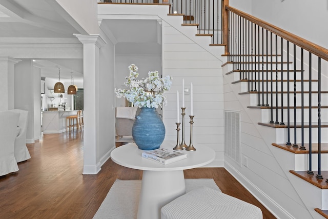 foyer entrance featuring dark wood-type flooring, ornamental molding, and ornate columns