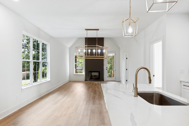 kitchen with light wood-type flooring, hanging light fixtures, vaulted ceiling, light stone counters, and sink