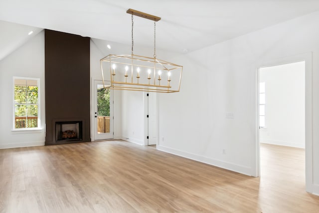 unfurnished living room with light wood-type flooring, a fireplace, an inviting chandelier, and vaulted ceiling