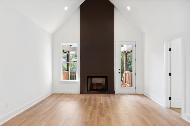 unfurnished living room with a large fireplace, a healthy amount of sunlight, light hardwood / wood-style floors, and high vaulted ceiling