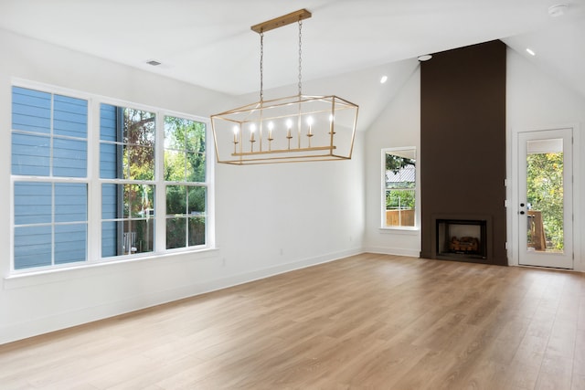 unfurnished living room featuring lofted ceiling, a fireplace, a notable chandelier, and light hardwood / wood-style floors