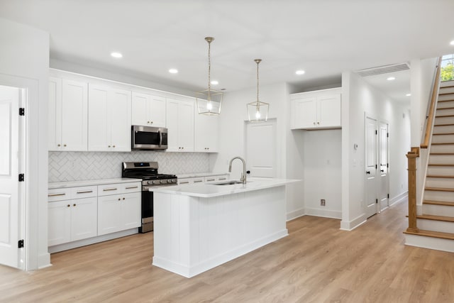 kitchen with decorative light fixtures, white cabinetry, stainless steel appliances, an island with sink, and sink