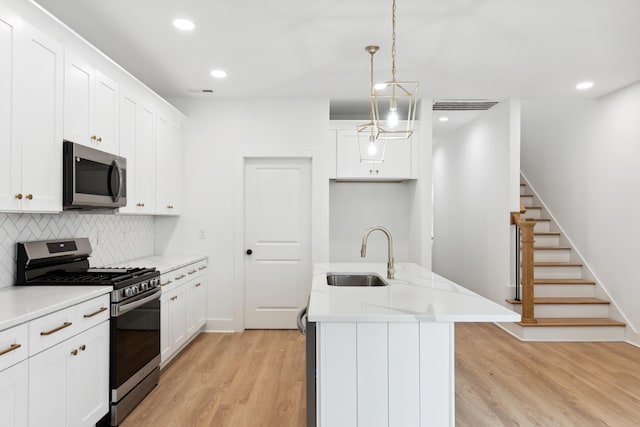 kitchen with an island with sink, appliances with stainless steel finishes, pendant lighting, white cabinets, and sink