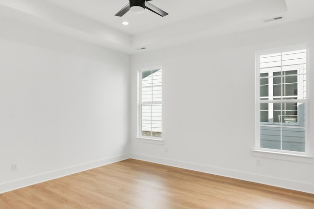 empty room with light hardwood / wood-style floors, a raised ceiling, and ceiling fan