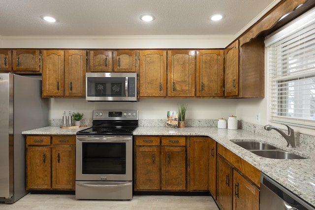 kitchen featuring light stone counters, sink, appliances with stainless steel finishes, and ornamental molding