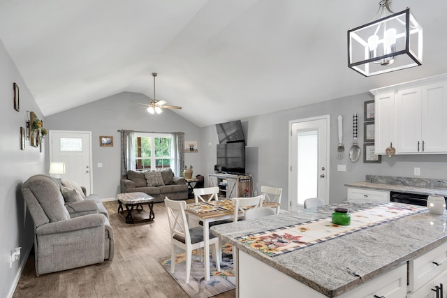 kitchen featuring ceiling fan with notable chandelier, light stone countertops, white cabinets, lofted ceiling, and light wood-type flooring