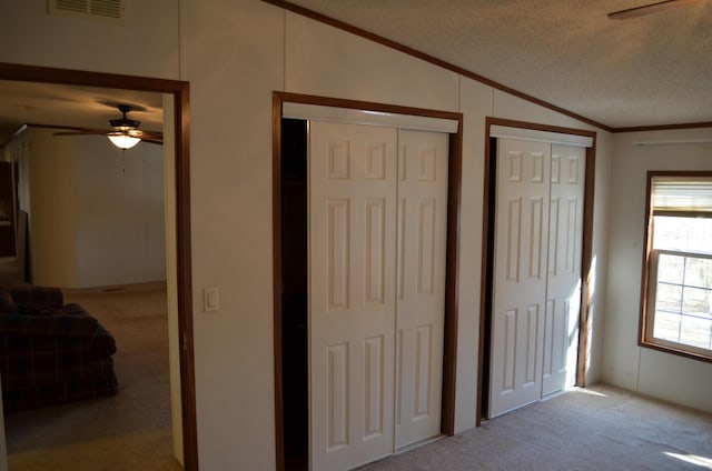 unfurnished bedroom featuring a textured ceiling, two closets, vaulted ceiling, ceiling fan, and light colored carpet