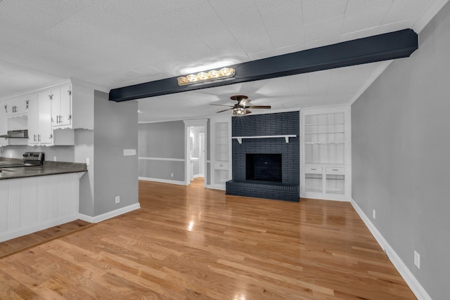 unfurnished living room with beamed ceiling, a fireplace, built in features, ceiling fan, and light hardwood / wood-style flooring