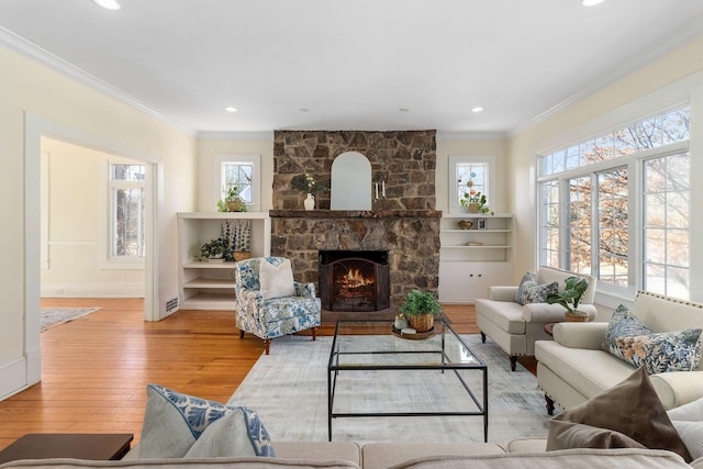 living room with ornamental molding, a stone fireplace, and light hardwood / wood-style floors