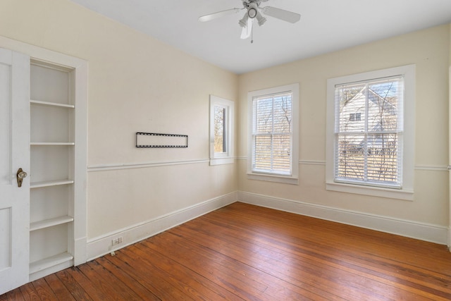 spare room featuring built in shelves, wood-type flooring, and ceiling fan