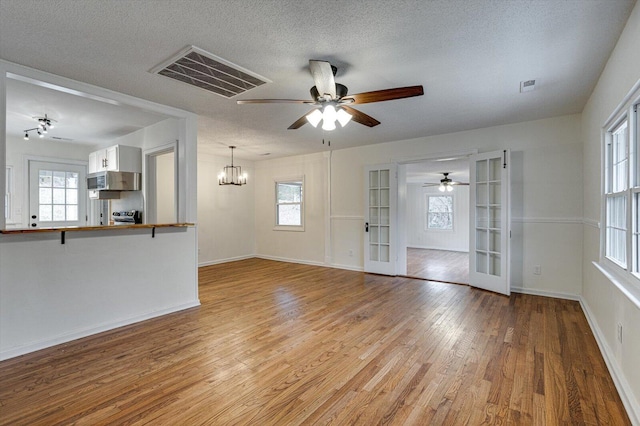 unfurnished living room featuring light wood-type flooring, plenty of natural light, a textured ceiling, and french doors