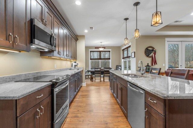 kitchen with a center island with sink, appliances with stainless steel finishes, decorative light fixtures, light stone countertops, and sink