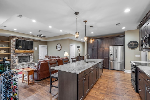 kitchen with sink, an island with sink, a kitchen breakfast bar, stainless steel appliances, and light stone counters