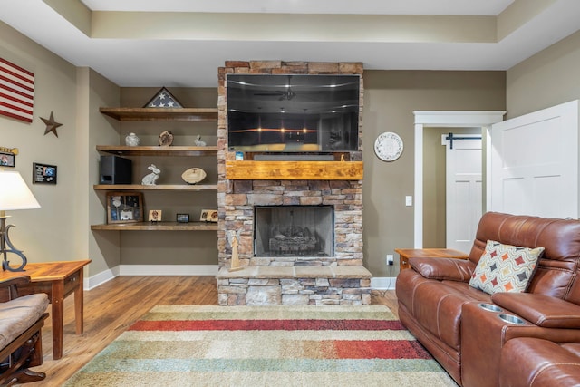 living room featuring built in shelves, a stone fireplace, and light wood-type flooring