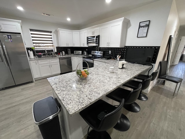 kitchen with a breakfast bar area, white cabinets, light wood-type flooring, and stainless steel appliances