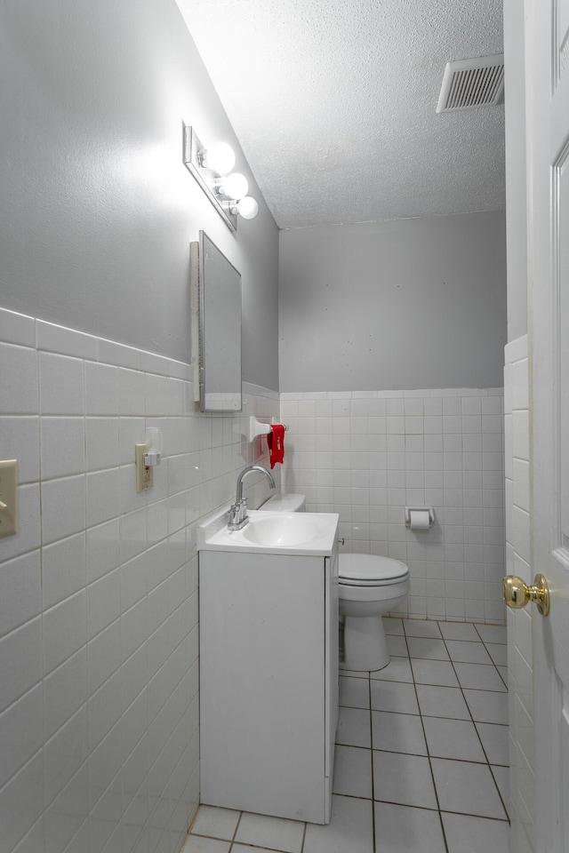 bathroom featuring tile patterned flooring, tile walls, vanity, a textured ceiling, and toilet