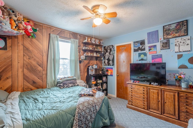 bedroom featuring light carpet, a textured ceiling, ceiling fan, and wood walls