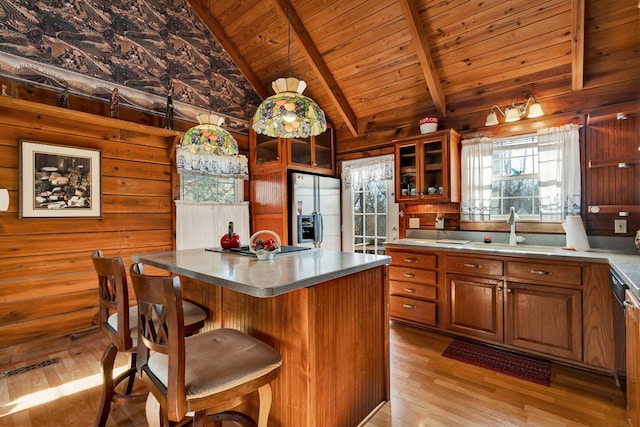 kitchen with stainless steel refrigerator with ice dispenser, sink, light wood-type flooring, wooden ceiling, and wood walls