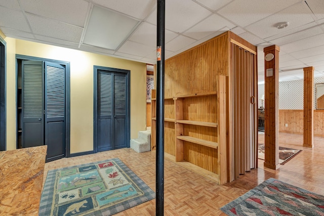 interior space featuring light parquet floors, a drop ceiling, and wood walls