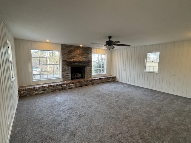 unfurnished living room with dark colored carpet, a healthy amount of sunlight, and a fireplace