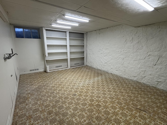 basement featuring a paneled ceiling, built in features, and carpet flooring