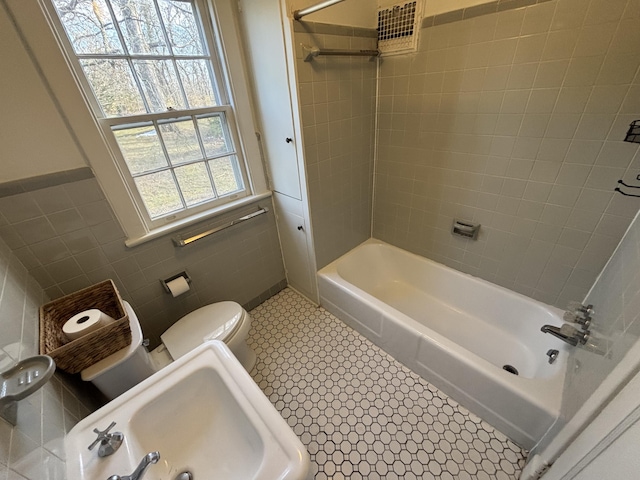 full bathroom featuring toilet, tiled shower / bath combo, tile patterned flooring, tile walls, and sink