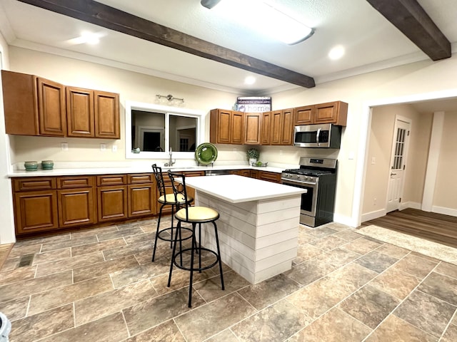 kitchen with appliances with stainless steel finishes, a kitchen island, a kitchen breakfast bar, sink, and beam ceiling