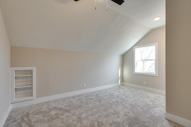 additional living space featuring light carpet, built in shelves, lofted ceiling, and a textured ceiling