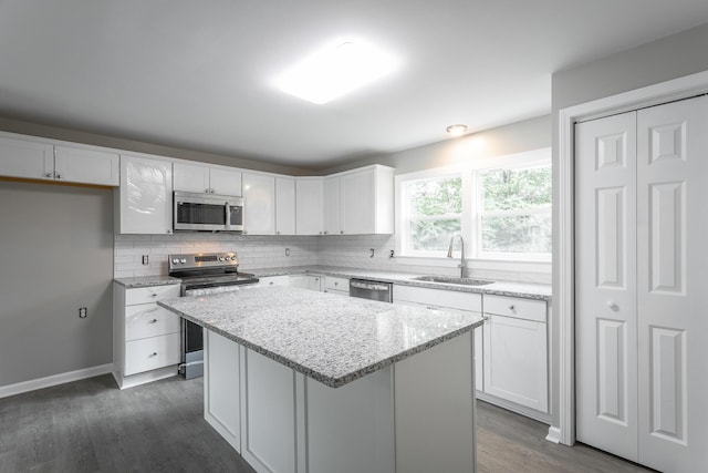 kitchen with appliances with stainless steel finishes, white cabinetry, sink, a center island, and light stone countertops