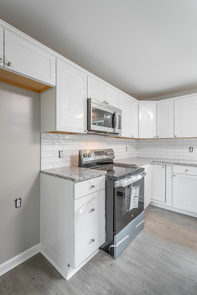 kitchen with appliances with stainless steel finishes, tasteful backsplash, white cabinets, light stone counters, and light wood-type flooring