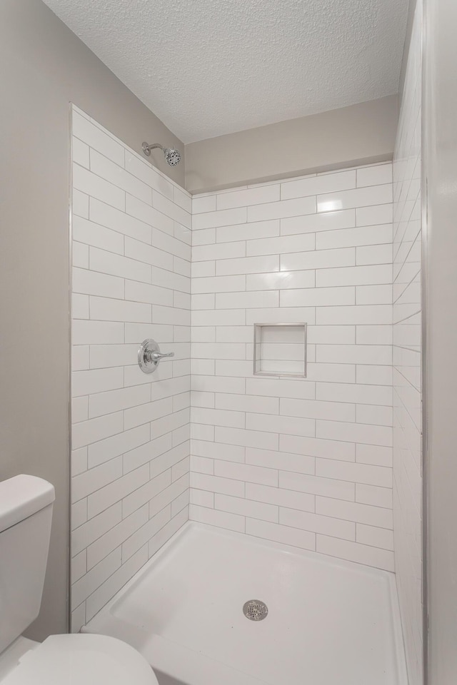 bathroom featuring a textured ceiling, toilet, and tiled shower