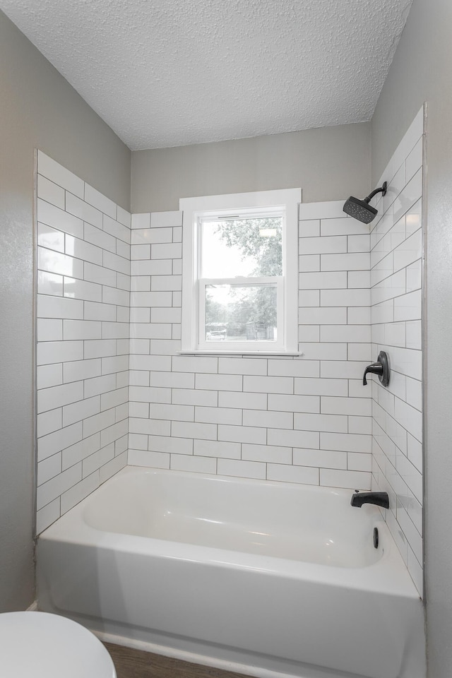 bathroom featuring tiled shower / bath combo, a textured ceiling, and toilet