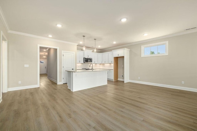 1691 Whisper Winds Ln Unit 35, Ooltewah, TN 37363 - kitchen with stainless steel microwave, a center island with sink, ornamental molding, white cabinetry, and light wood-style flooring
