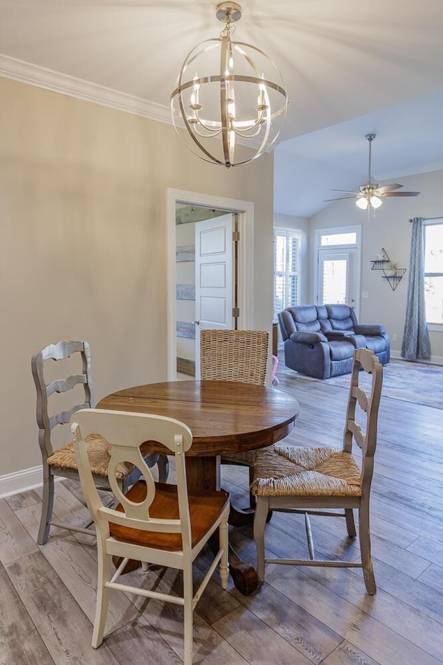 dining space with crown molding, light wood-type flooring, ceiling fan with notable chandelier, and lofted ceiling