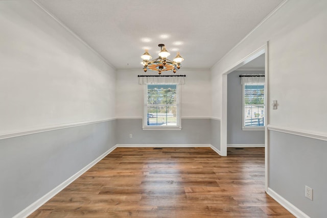 unfurnished dining area featuring crown molding, a chandelier, wood-type flooring, and plenty of natural light