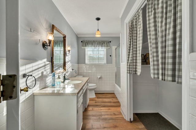 full bathroom featuring toilet, combined bath / shower with glass door, tile walls, ornamental molding, and vanity