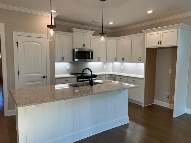 kitchen with a kitchen island with sink, white cabinetry, and pendant lighting