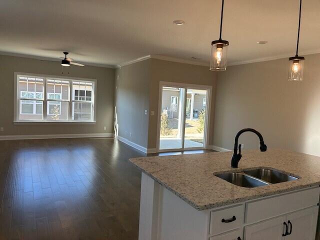 kitchen with light stone countertops, white cabinets, sink, hanging light fixtures, and ceiling fan