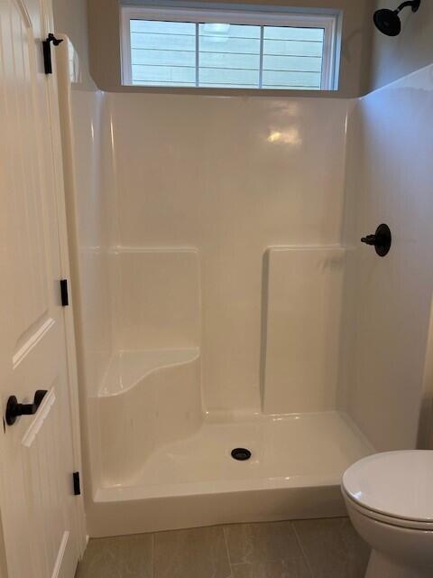 bathroom with toilet, a shower, and tile patterned floors