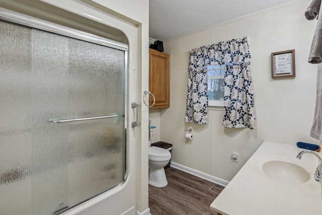 full bathroom featuring a textured ceiling, wood-type flooring, toilet, combined bath / shower with glass door, and crown molding