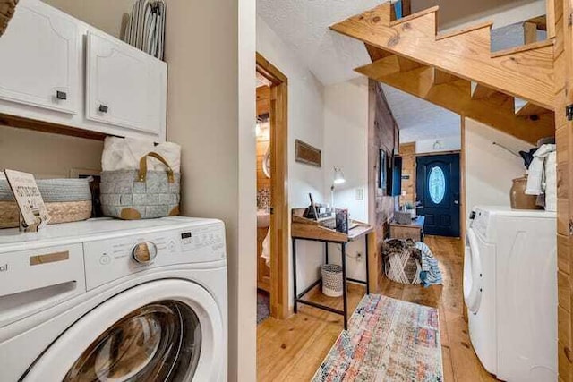 washroom featuring cabinets, light wood-type flooring, a textured ceiling, and independent washer and dryer