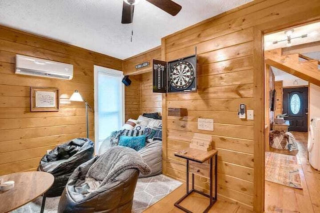 interior space featuring a wall mounted air conditioner, a textured ceiling, ceiling fan, and wood walls