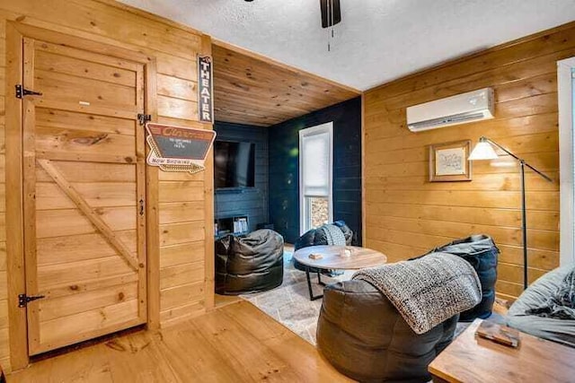 living area with wood-type flooring, an AC wall unit, ceiling fan, and wooden walls