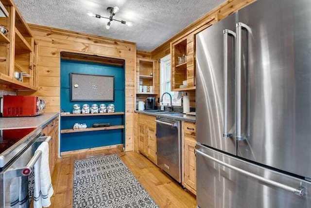 kitchen with appliances with stainless steel finishes, rail lighting, sink, light wood-type flooring, and a textured ceiling