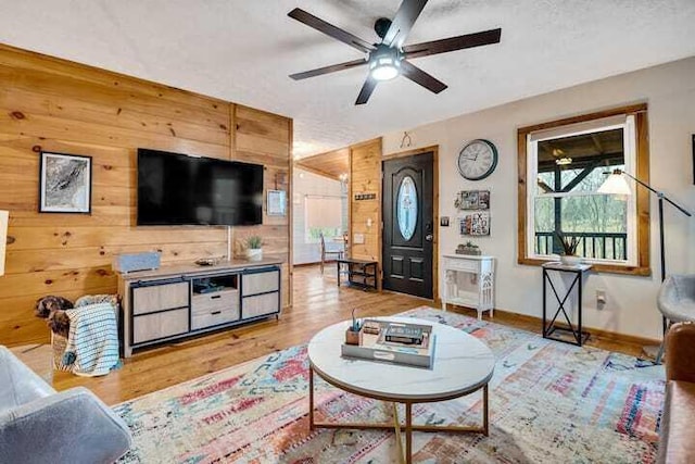 living room featuring ceiling fan, light hardwood / wood-style floors, a textured ceiling, and wood walls