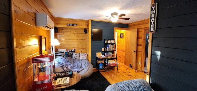 bedroom with wood-type flooring, a textured ceiling, an AC wall unit, wooden walls, and ceiling fan