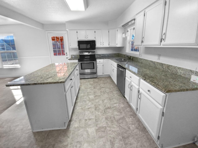 kitchen featuring white cabinets, appliances with stainless steel finishes, a kitchen island, and dark stone countertops